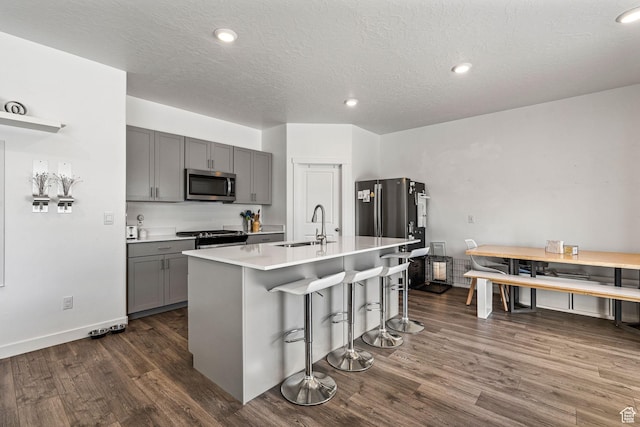 kitchen with gray cabinetry, stainless steel appliances, a breakfast bar, light countertops, and an island with sink
