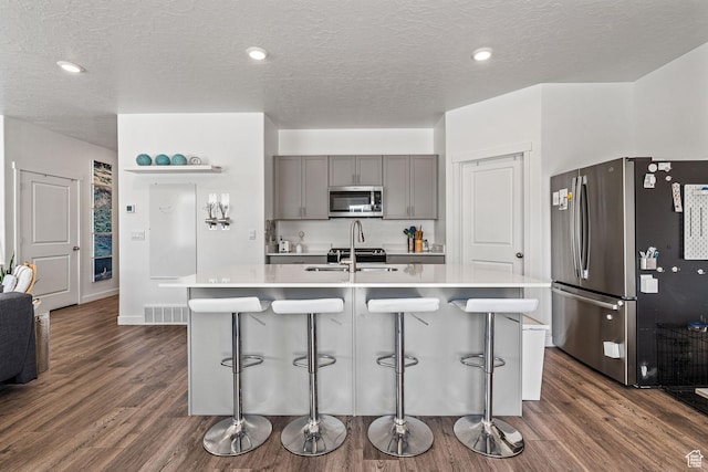 kitchen with stainless steel appliances, light countertops, a center island with sink, and gray cabinetry