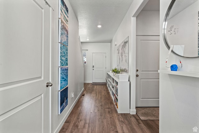 hall featuring a textured ceiling, dark wood finished floors, and baseboards