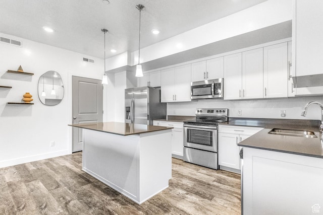 kitchen featuring white cabinets, dark countertops, hanging light fixtures, stainless steel appliances, and a sink