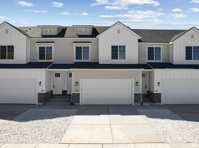 view of front facade with an attached garage, a shingled roof, driveway, stone siding, and board and batten siding