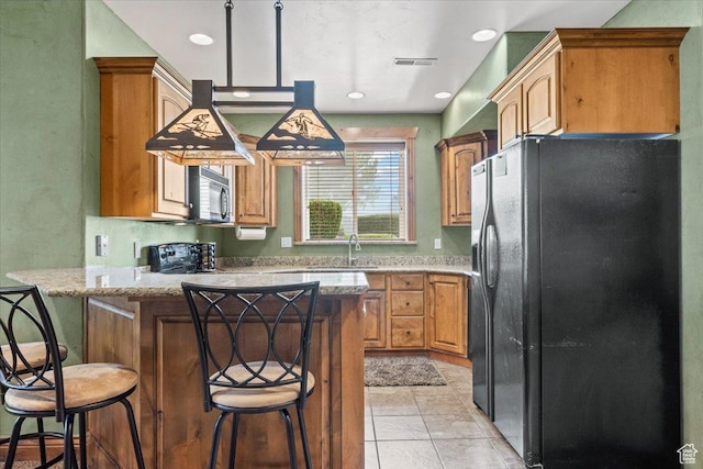 kitchen with light tile patterned floors, a kitchen bar, a peninsula, black appliances, and a sink