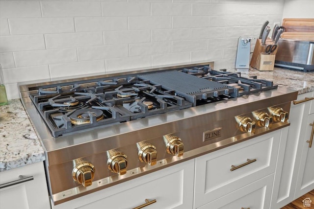 details featuring stainless steel gas cooktop, backsplash, white cabinetry, and light stone counters