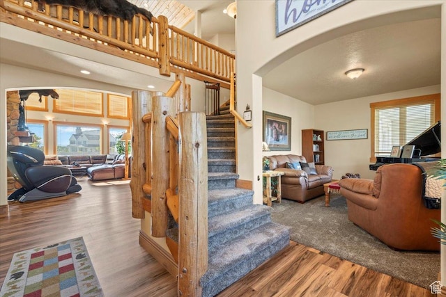 staircase with arched walkways, a towering ceiling, and wood finished floors