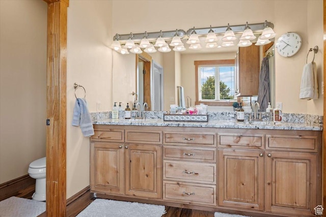 bathroom featuring baseboards, a sink, double vanity, and toilet