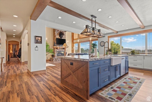 kitchen featuring beam ceiling, arched walkways, wood finished floors, and a textured ceiling