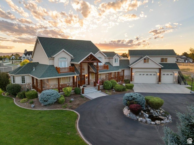 view of front of home featuring concrete driveway, a balcony, stucco siding, stone siding, and a front yard
