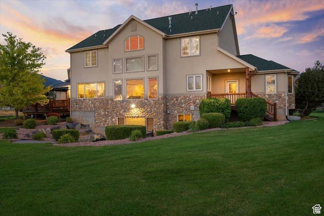back of property featuring a wooden deck, stucco siding, stone siding, and a lawn