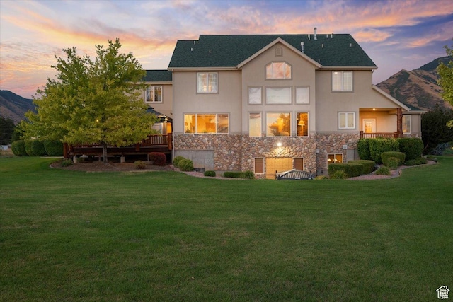 rear view of house with a yard, a deck with mountain view, stone siding, and stucco siding