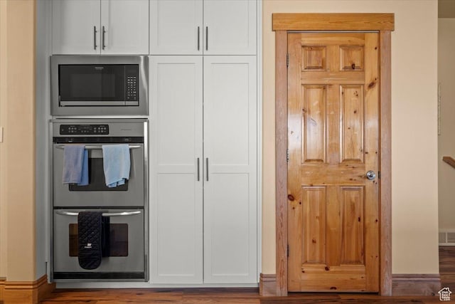 kitchen with white cabinetry, built in microwave, visible vents, double oven, and wood finished floors