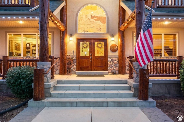 property entrance featuring a porch, french doors, stone siding, and stucco siding
