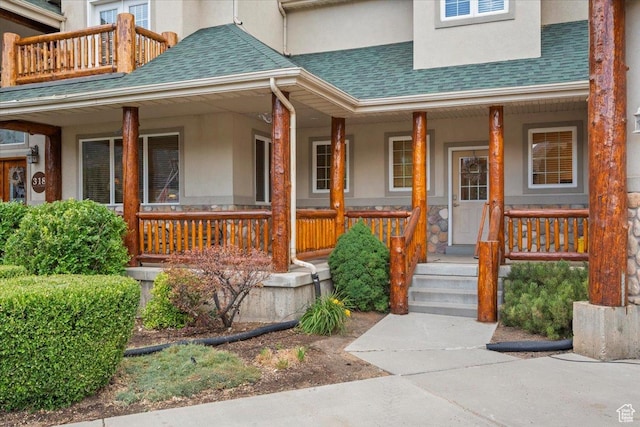 entrance to property featuring a porch, stucco siding, a balcony, and roof with shingles