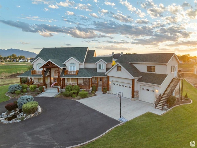 view of front of home with a front yard, a balcony, an attached garage, a shingled roof, and driveway