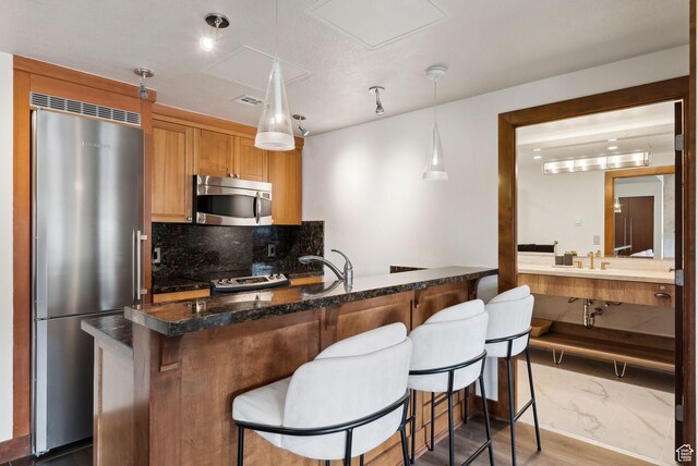 3720 N Sundial Ct Unit C207, Park City, UT 84098 - kitchen with appliances with stainless steel finishes, decorative backsplash, a kitchen bar, pendant lighting, and brown cabinets