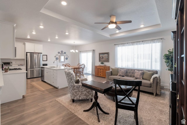 living room with a tray ceiling, light wood-style flooring, and recessed lighting