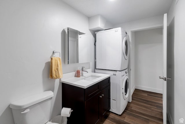 laundry room with stacked washer and clothes dryer, dark wood finished floors, a sink, laundry area, and baseboards