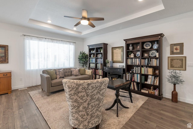 living room with recessed lighting, wood finished floors, a ceiling fan, baseboards, and a tray ceiling