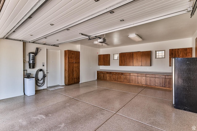 garage featuring baseboards, a garage door opener, and freestanding refrigerator