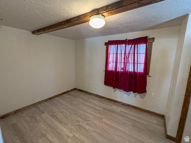 unfurnished room with a textured ceiling, beamed ceiling, wood finished floors, and baseboards