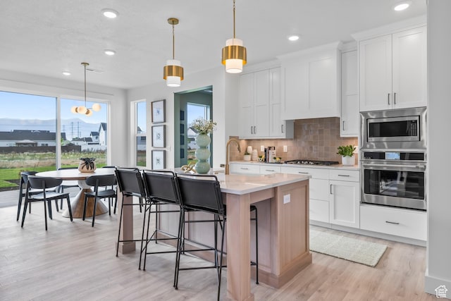 2452 W 2950 N Unit 112, Farr West, UT 84404 - kitchen with white cabinets, an island with sink, appliances with stainless steel finishes, decorative light fixtures, and backsplash