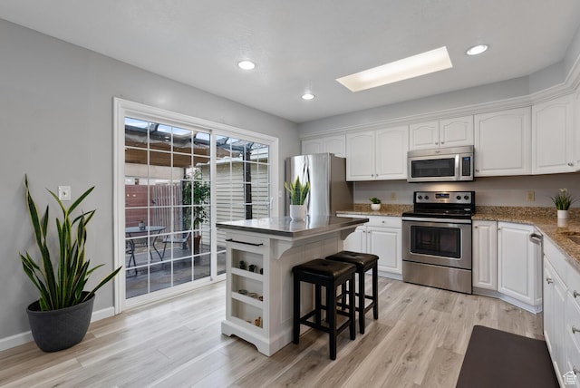 kitchen featuring light wood-style flooring, appliances with stainless steel finishes, white cabinets, a kitchen island, and a kitchen breakfast bar