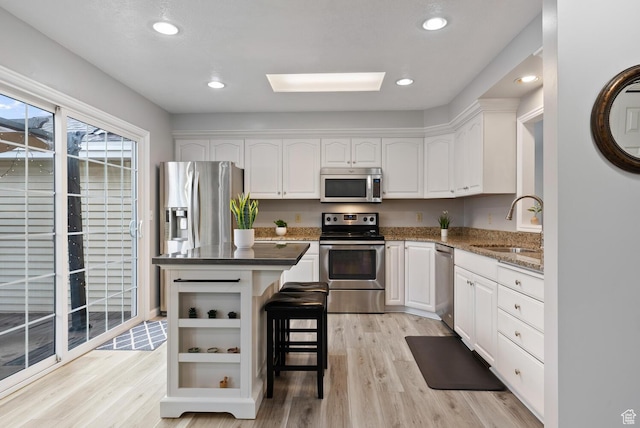 kitchen with dark countertops, a kitchen island, a breakfast bar, stainless steel appliances, and white cabinetry