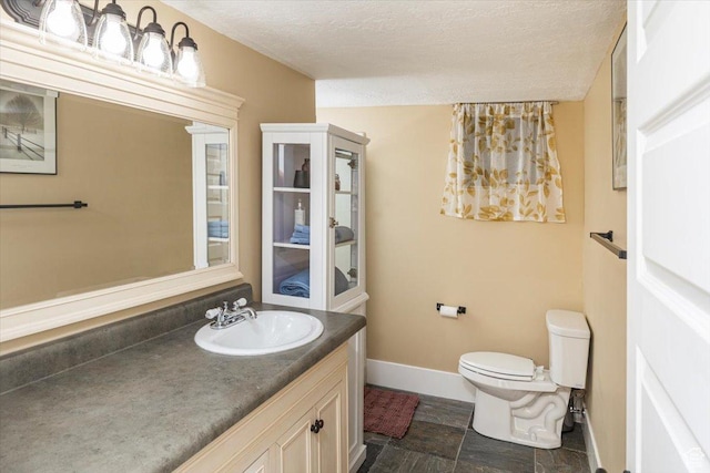 bathroom with toilet, vanity, baseboards, and a textured ceiling
