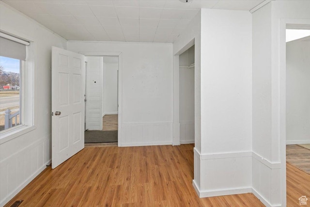 unfurnished bedroom featuring a closet, light wood-style flooring, and wainscoting