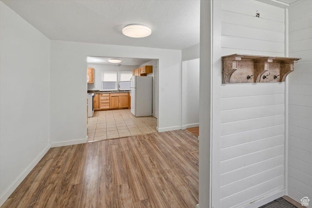 kitchen featuring light wood finished floors, dark countertops, baseboards, freestanding refrigerator, and a textured ceiling