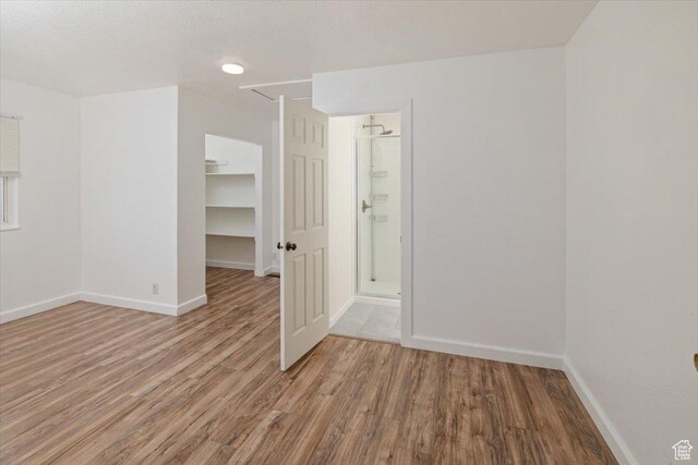 unfurnished bedroom with a walk in closet, wood finished floors, and baseboards