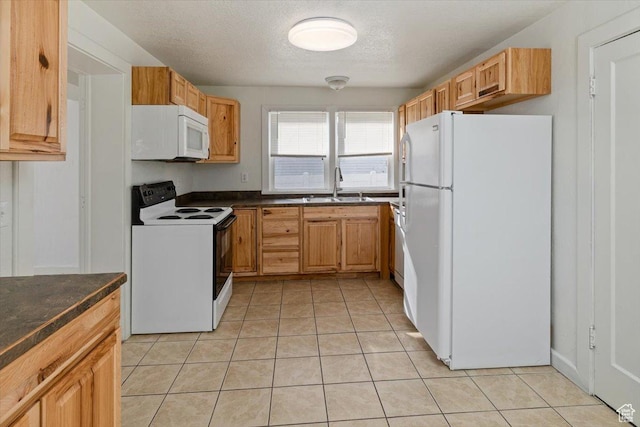 kitchen featuring white appliances, light tile patterned floors, dark countertops, and a sink