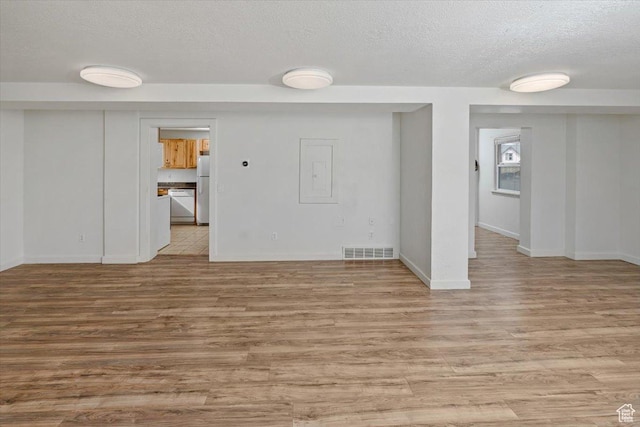 interior space featuring visible vents, baseboards, a textured ceiling, and light wood finished floors