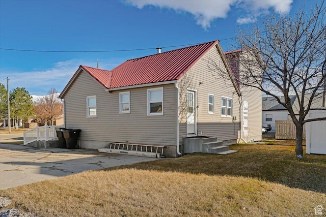 back of property featuring entry steps, fence, a lawn, and metal roof