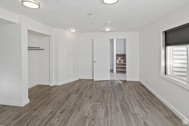 unfurnished bedroom featuring visible vents, baseboards, wood finished floors, a closet, and a textured ceiling