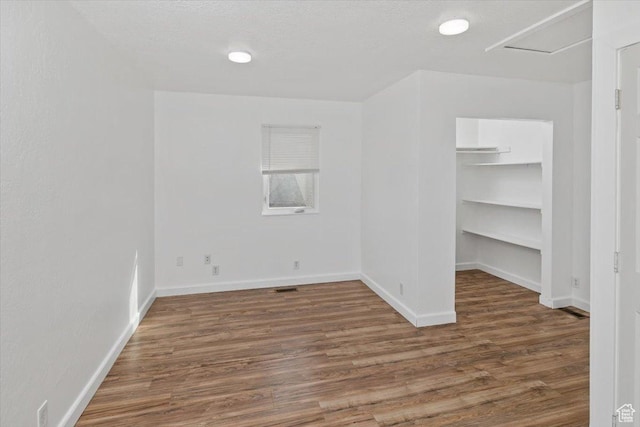 interior space featuring baseboards, a textured ceiling, wood finished floors, and a spacious closet