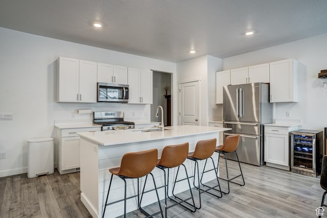 kitchen featuring a sink, light countertops, a kitchen breakfast bar, stainless steel appliances, and wine cooler