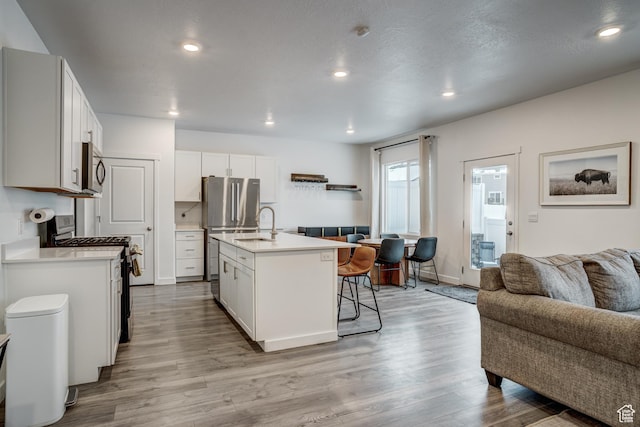 kitchen with appliances with stainless steel finishes, light countertops, open floor plan, a breakfast bar, and light wood-style flooring