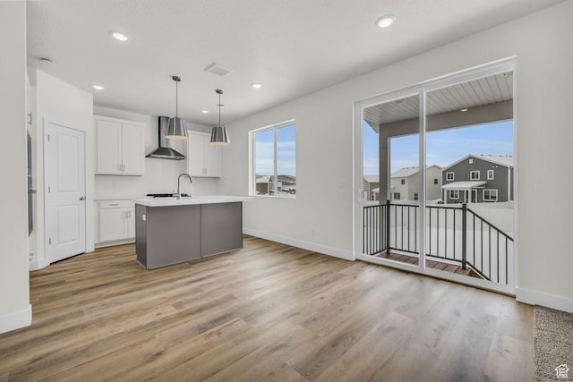 7181 Woods Rose Dr, Park City, UT 84098 - kitchen with wall chimney range hood, white cabinets, an island with sink, light wood finished floors, and recessed lighting