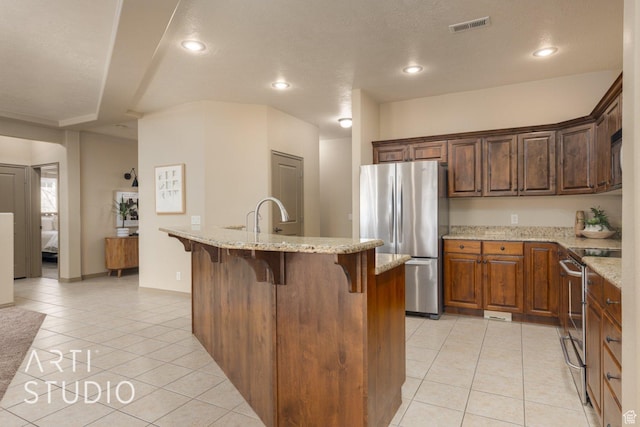 1109 N Ventana Dr, Washington, UT 84780 - kitchen with light tile patterned flooring, stainless steel appliances, visible vents, a kitchen bar, and a center island with sink