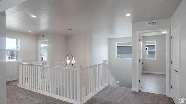 corridor featuring light colored carpet, visible vents, an inviting chandelier, a textured ceiling, and an upstairs landing