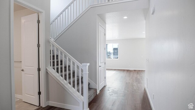 stairway with baseboards, wood finished floors, and recessed lighting