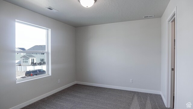 empty room with a textured ceiling, carpet flooring, visible vents, and baseboards