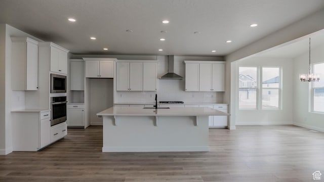 kitchen with white cabinets, a sink, wall chimney range hood, an island with sink, and stainless steel appliances