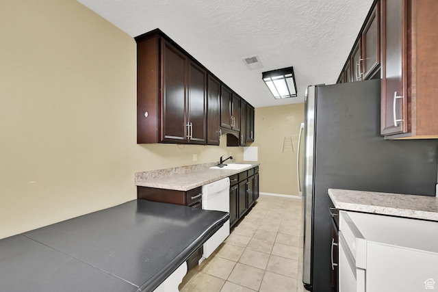 kitchen with light countertops, light tile patterned flooring, freestanding refrigerator, baseboards, and dishwasher
