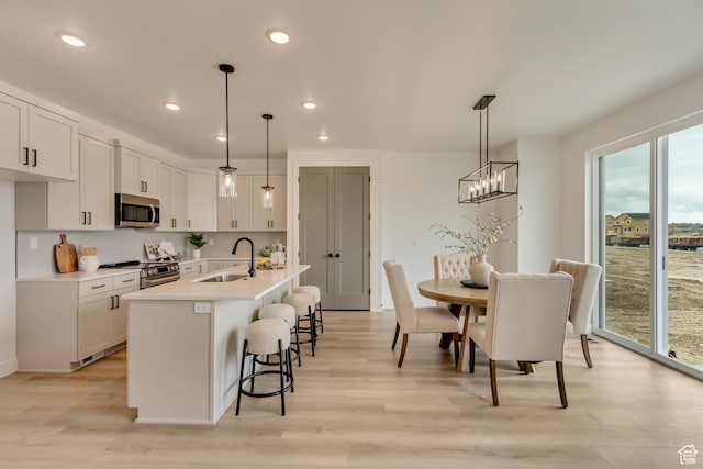 kitchen with stainless steel appliances, a breakfast bar, light countertops, a sink, and light wood-style flooring