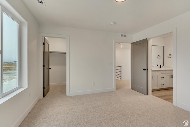 unfurnished bedroom featuring ensuite bath, baseboards, visible vents, and light colored carpet