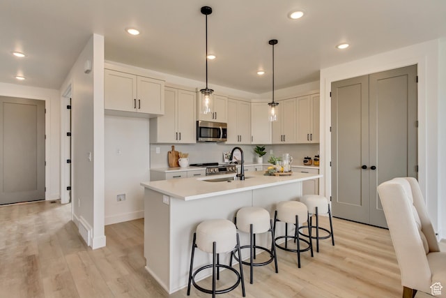 kitchen featuring a sink, stainless steel microwave, light wood-style floors, a kitchen bar, and light countertops