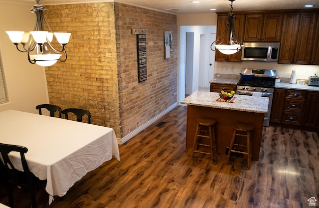 kitchen featuring brick wall, a kitchen island, dark wood-type flooring, stainless steel appliances, and pendant lighting