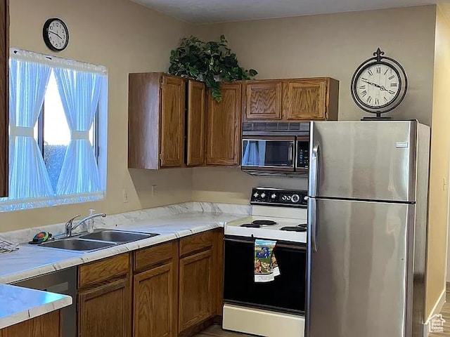 kitchen featuring light countertops, appliances with stainless steel finishes, a sink, and brown cabinets