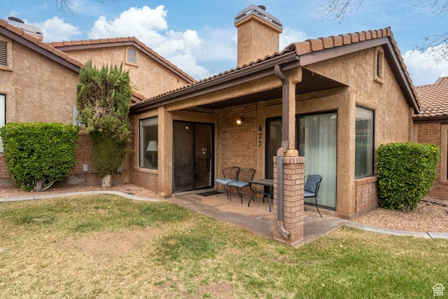 rear view of property with a patio, a tile roof, a yard, stucco siding, and a chimney